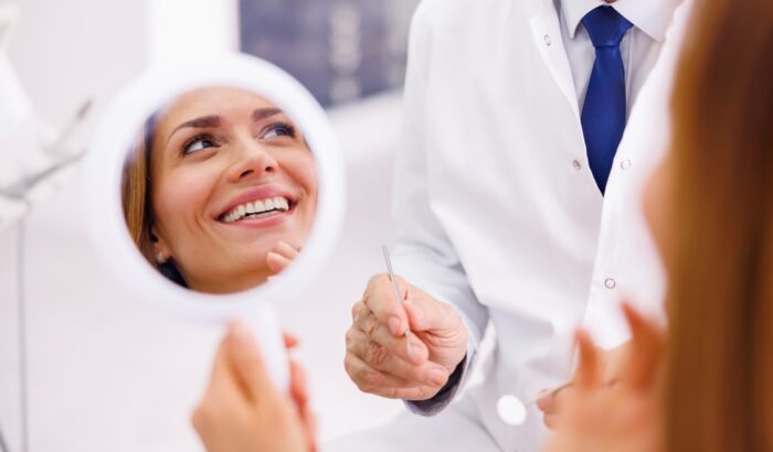 Woman,Looking,In,The,Mirror,And,Smiling,After,Checkup,At